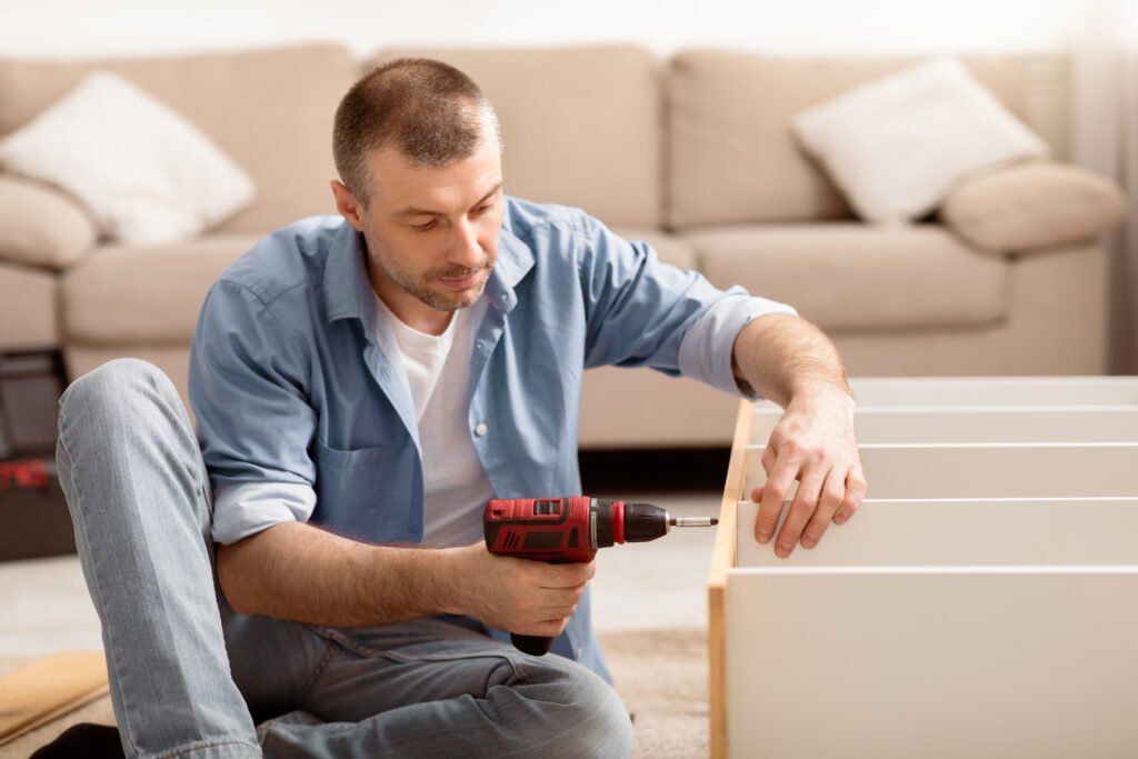 Hombre con taladro eléctrico montando estantería de madera amueblando habitación interior